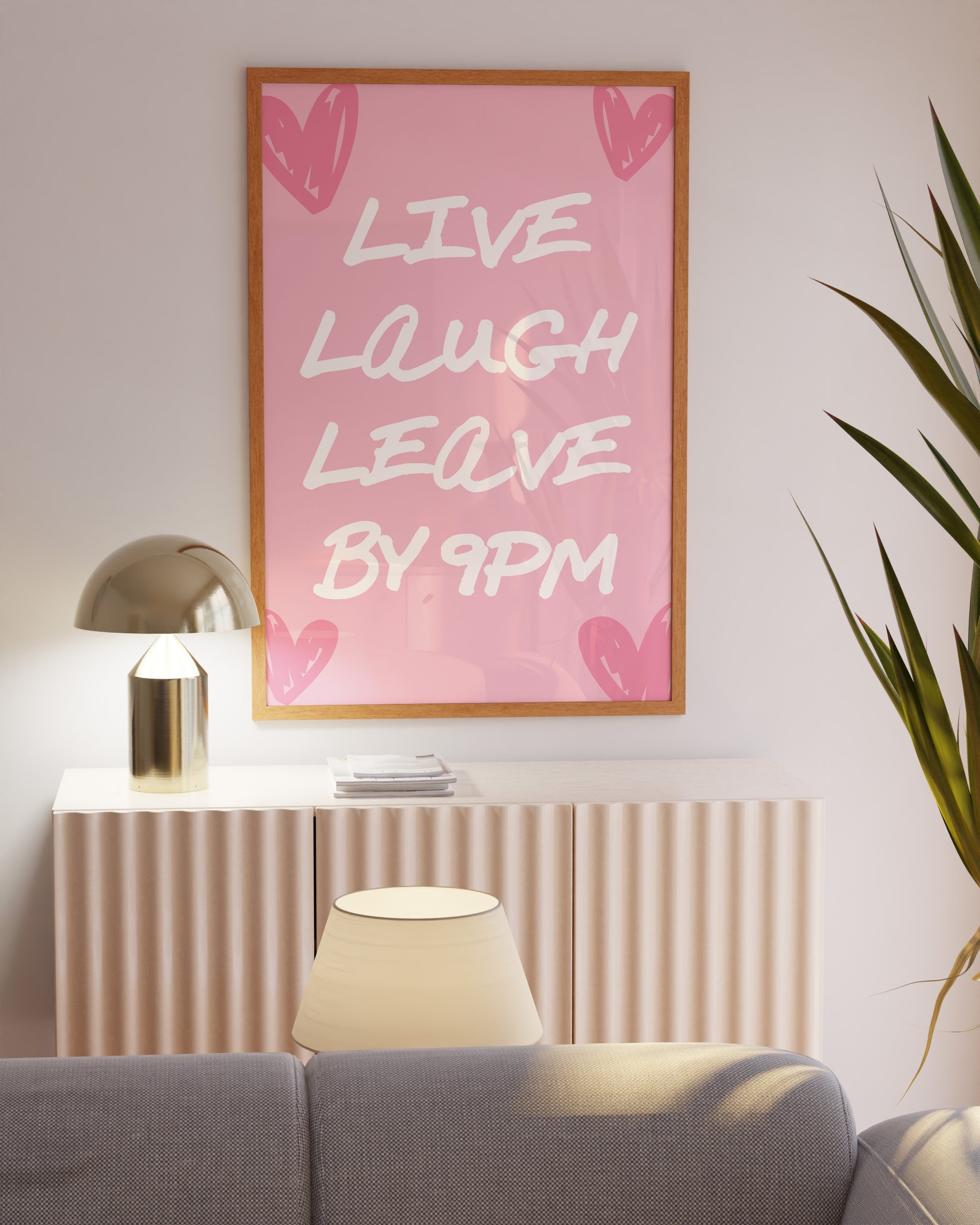 Minimalist pink wall art print with the funny quote 'Live Laugh Leave by 9PM' in white brushstroke font, leaning against a stylish modern shelf.